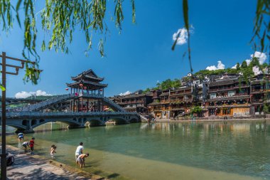 Feng Huang, Çin - Ağustos 2019: Antik Antik Antik Kent olarak bilinen Antik Kentte, Tuojiang Nehri üzerindeki kemerli köprünün yanında çocuklar ve yerel sakinler yıkanıyor, su sıçratıyorlar ve eğleniyorlar