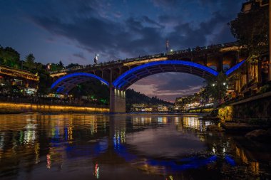 Feng Huang, Çin - Ağustos 2019: Günbatımından sonra Tuo Jiang nehri üzerindeki yol köprüsü ve antik Fenghuang kasabasındaki ahşap evler