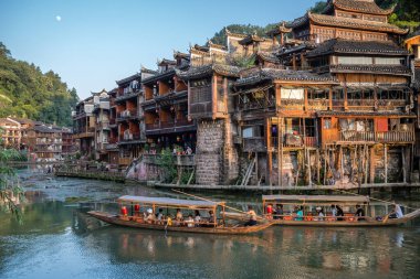 Feng Huang, Çin - Ağustos 2019: Fenghuang Eski Kasabası 'nın merkezinden akan Tuo nehrinin kıyısında inşa edilmiş eski tahta evlerin arasında seyir halindeki eski ahşap turist tekneleri