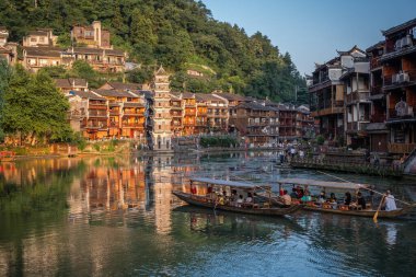 Feng Huang, Çin - Ağustos 2019: Fenghuang Eski Kasabası 'nın merkezinden akan Tuo nehrinin kıyısında inşa edilmiş eski tahta evlerin arasında seyir halindeki eski ahşap turist tekneleri
