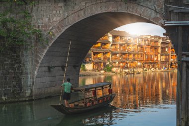 Feng Huang, Çin - Ağustos 2019: Feng Huang, Çin - Ağustos 2019: Eski tarihi ahşap turizm teknesi Tuo nehri üzerindeki ikonik tarihi bir köprü altında yüzüyor, Fenghuang Eski Kasabası 'nın merkezinden geçiyor.