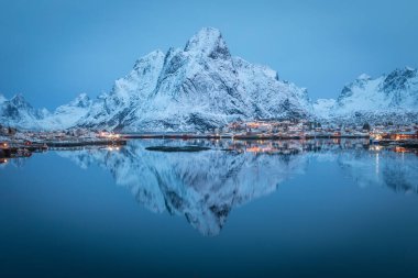 Büyük karla kaplı dağ uzak kuzey fiyordun sakin ve soğuk sularına yansıyor. Şafakta balıkçı köyü. Lofoten 'dan huzur sahnesi, Kuzey Kutbu dairesi..