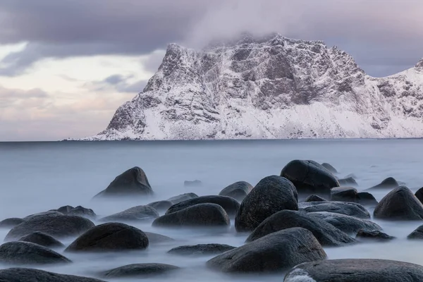 Norveç, Lofoten 'deki Uttakleiv plajının uzun süreli görüntüsü. Yumuşak deniz ve kayalar. Arkaplan karla kaplıydı. Sakin kış sahnesi.