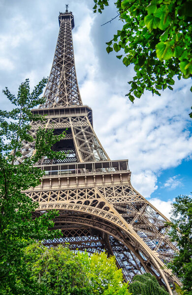 A fragment of a tall Eiffel tower with tree leaves and clouds