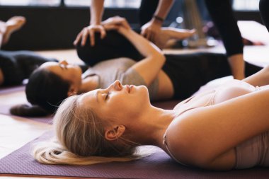 Yoga yapan bir grup genç, spor salonunda antrenörle yoga minderlerinde yalan söylüyor. Rahatlama ve meditasyon kavramı.