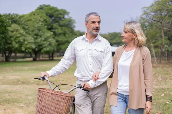 Couple elderly relaxing at park walking with bike and talking together in morning