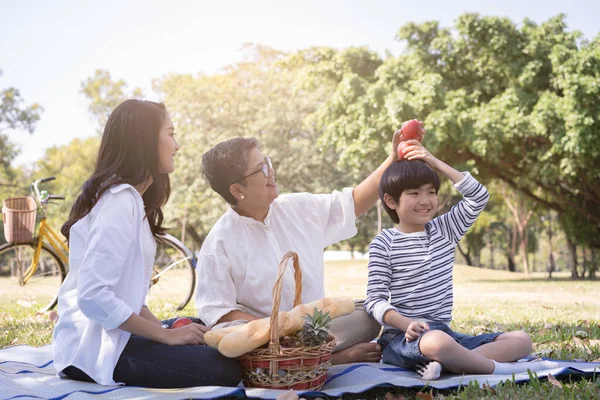 Asian family with son sitting hold apple above his head in the public park