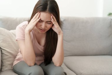 Asyalı kadınlar evlerindeki kanepede otururken ellerini başlarının üstüne koyuyorlar, genç kadınların migren, sağlık ve hastalık konsepti yüzünden şiddetli baş ağrıları var.