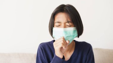 Asyalı kız semptomları öksürür ve kanepede otururken tıbbi maske takar, Asya çocuğu grip salgını ya da evdeki oturma odasında Cvid-19 salgını takar. Sağlık ve hastalık konsepti