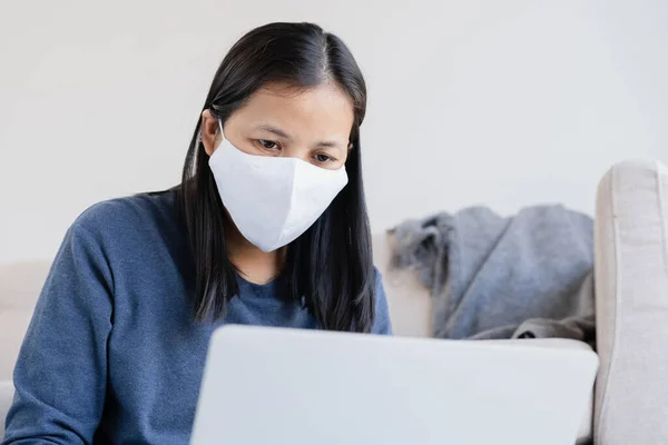 Asian women wearing a protection mask epidemic of flu or covid-19 in the living room at home. Asia woman using a laptop and work from home. Health and illness concept