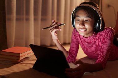 Mutlu Asyalı kız, öğretmeniyle çevrimiçi video konferansı okuyor geceleri yatak odasındaki tablette, Asyalı çocuk izleme ve eğitim mesafesi bilgisayarda, evde öğrenme kavramını kavrıyor.