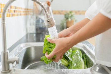 Yakın plan Asyalı kadınlar mutfakta sebze yıkıyor ve sabah evde marul hazırlıyorlar.