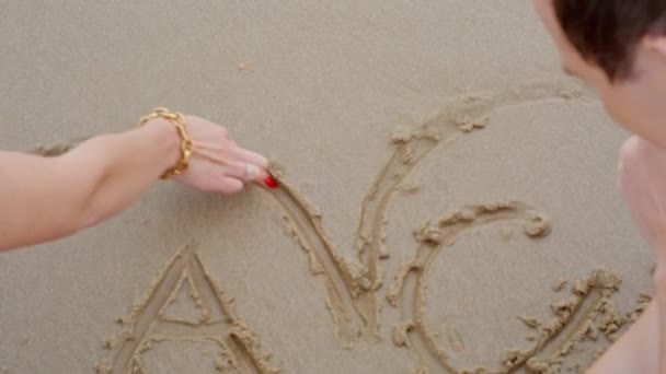 Chico y una chica en la playa dibujar corazón — Vídeo de stock