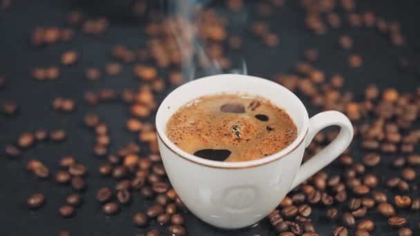 Taza con bebida caliente en granos de café tostados. Movimiento lento — Vídeos de Stock