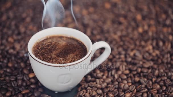 Tasse avec boisson chaude sur grains de café torréfiés. Mouvement lent — Video