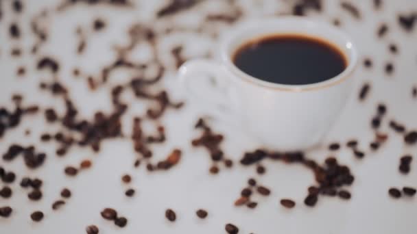 Taza de café blanco y granos de café sobre fondo blanco — Vídeos de Stock