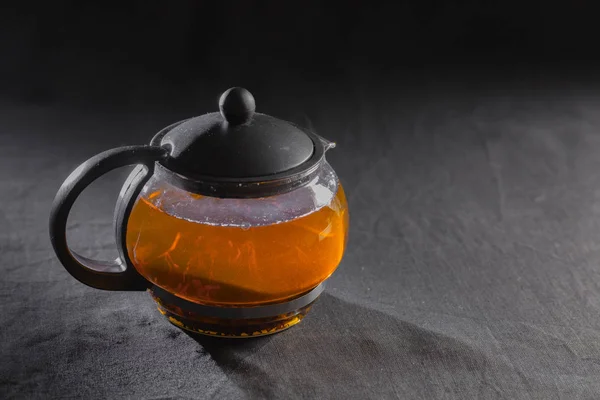 Черный чай в прозрачном чайнике на черном фоне — стоковое фото