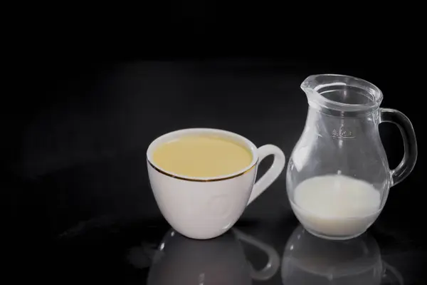 Café en una taza de leche blanca en una jarra pequeña sobre fondo negro — Foto de Stock