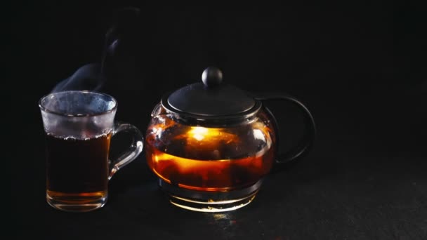 Té negro en una tetera transparente té en vidrio Copa sobre fondo negro — Vídeos de Stock