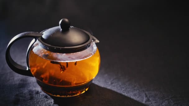 Черный чай в прозрачном чайнике на черном фоне — стоковое видео