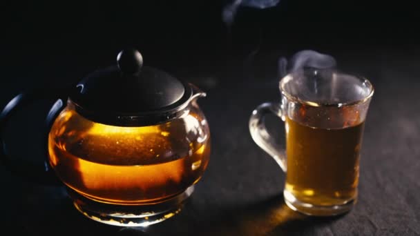 Schwarzer Tee in einer transparenten Teekanne Tee in Glasschale auf schwarzem Hintergrund — Stockvideo