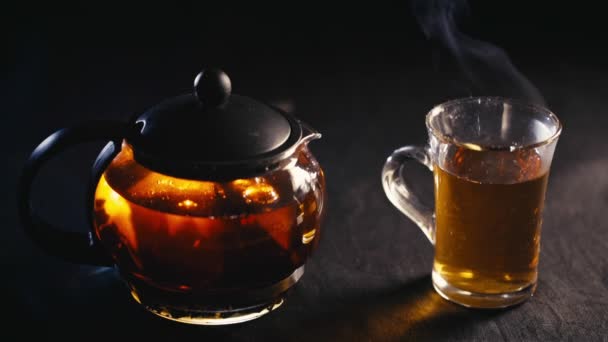 Zwarte thee in een transparante theepot thee in glazen beker op zwarte achtergrond — Stockvideo