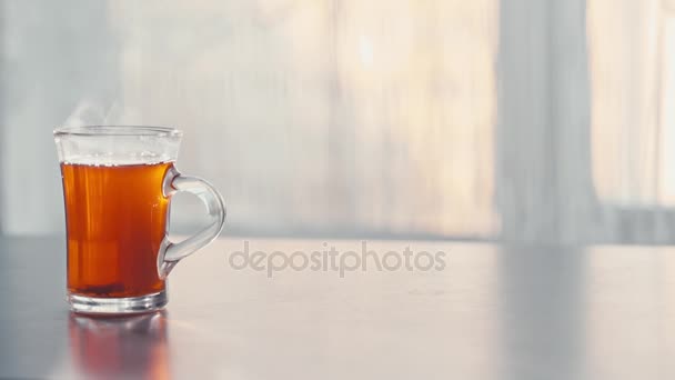 Una taza de té caliente al vapor en la mesa contra la ventana . — Vídeo de stock