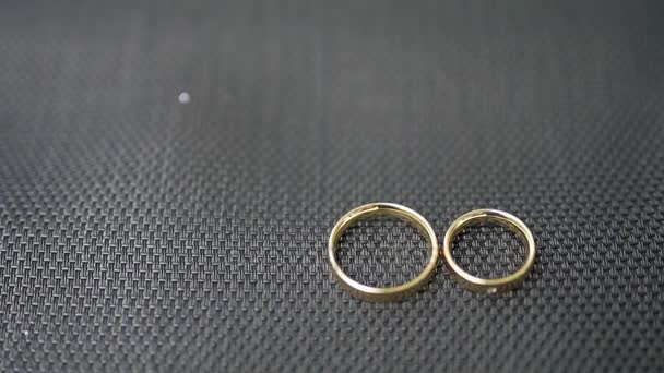 Anillos de boda se encuentran sobre un fondo negro — Vídeos de Stock