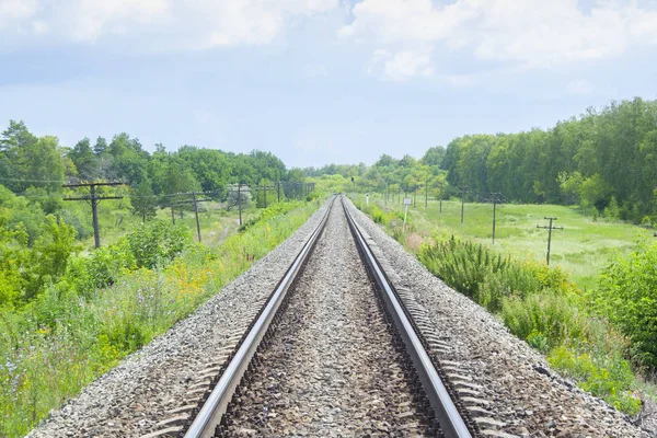 Un ferrocarril a través de los campos verdes de verano. Hermoso ferrocarril verde árbol paisaje cielo nubes. Hermoso paisaje. Transporte ferroviario . —  Fotos de Stock