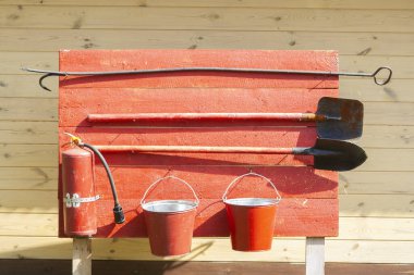 Kırmızı ahşap kalas üzerinde yangın korumalı aletler. Yangın söndürücü, kova, hurda ve kürek..