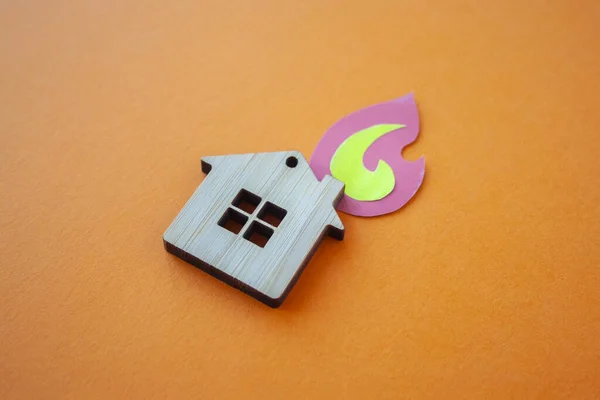Fire house, insurance and mortgage concept. Small wooden house toy and paper fire shape on orange background side view