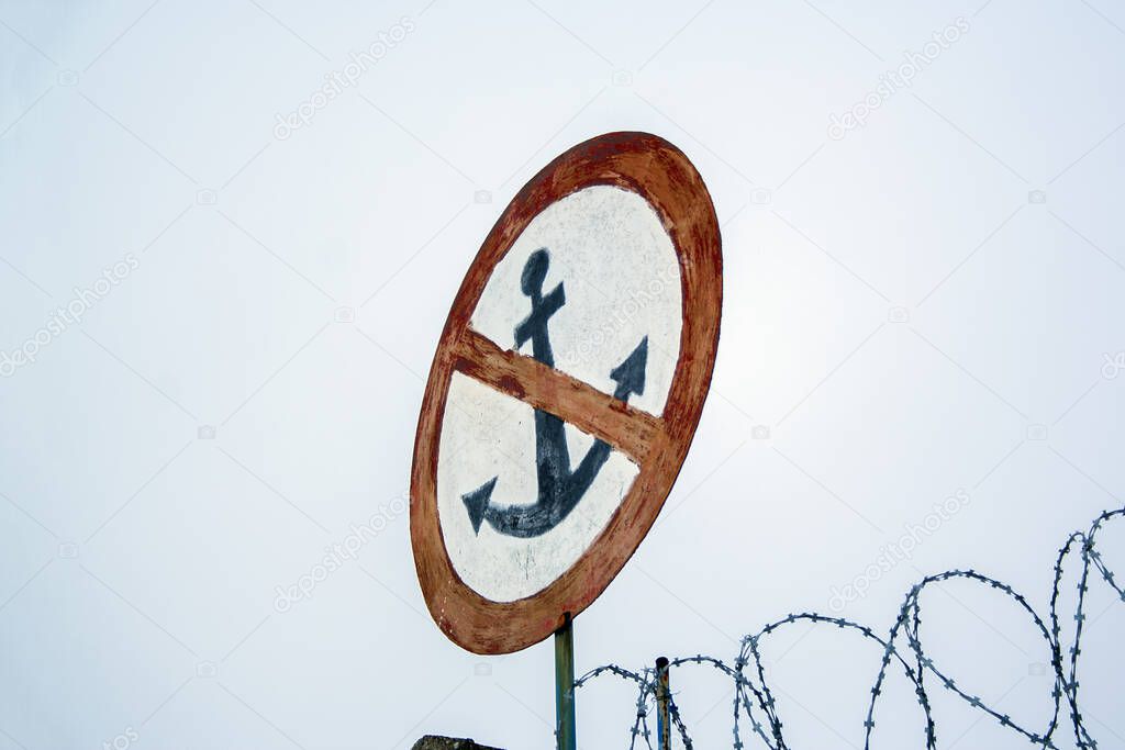 No anchor sign on grey sky backdrop with barbed wires
