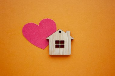 Aşk evi, sigorta ve ipotek, evlilik ve sevgililer günü konsepti. Küçük tahta ev oyuncağı ve kağıt kalp şeklinde turuncu arka plan manzaralı. 