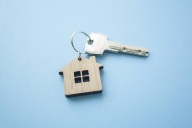 Anahtar ve ev şekilli anahtarlık düzeni mavi arka planda. Üst manzara, düz yatış. Gayrimenkul, sigorta konsepti, ipotek, satın alma evi, emlakçı