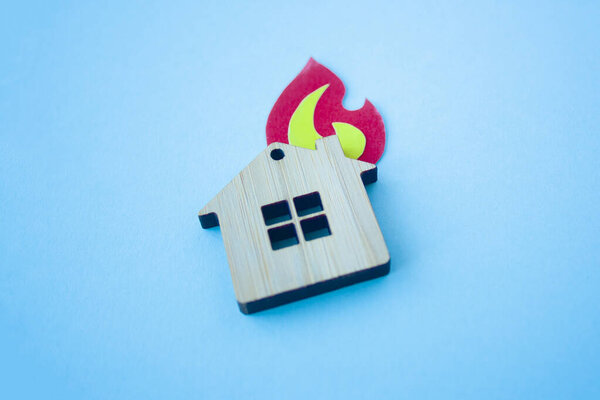 Концепция пожарной части, страхования и ипотеки. Маленькая деревянная игрушка дом и бумага форма огня на синем фоне вид сбоку с копировальным пространством
