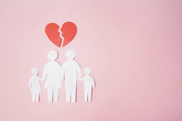 paper family cut out on bright pink background with broken heart above, family home, foster care, family mental health, divorce and family crisis concept