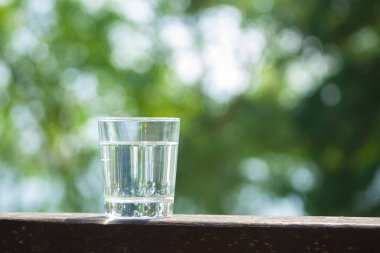 Su bardağı, güneş ışınlarındaki ahşap tahtanın üzerinde duruyor. Sıcak yaz günleri konseptinde susuzluk. Sağlıklı yaşam tarzı sembolü. Kopya alanı olan sağlıklı su içeceği