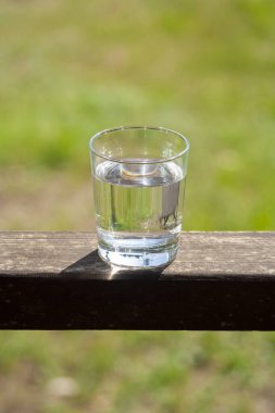 Su bardağı, güneş ışınlarındaki ahşap tahtanın üzerinde duruyor. Sıcak yaz günleri konseptinde susuzluk. Sağlıklı yaşam tarzı sembolü. Sağlıklı su dikey içer