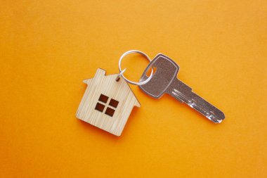Anahtar ve ev şekilli anahtarlık turuncu arka planda. Üst manzara, düz yatış. Gayrimenkul, sigorta konsepti, ipotek, satın alma evi, emlakçı