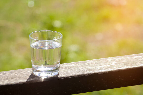 Water glass stands on wooden plank on sunbeams. Hydration at hot summer days concept. Healthy lifestyle symbol. Healthy water drink sunny