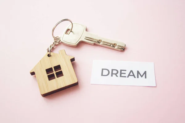 Wooden house toy and silver key on bright pink background with phrase quote Dream. Mortgage, house buy sell, investment, rent, realtor concept