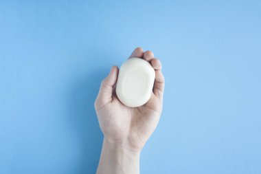 Bir erkeğin elindeki bir sabun parçası mavi arka planda üst bir görüntü. İnsan eli sabun tutar. Ellerini yıka. Bakteri ve virüslere karşı sabun. Koronavirüsle savaşmak için hijyen ve kısırlığa uyum.