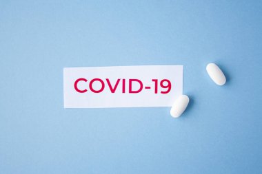 Mavi arka planda, üzerinde iki beyaz tablet bulunan Covid-19 yazısından alıntı. Coronavirus tedavisi konsepti. İlaçlar, virüs aşısı..