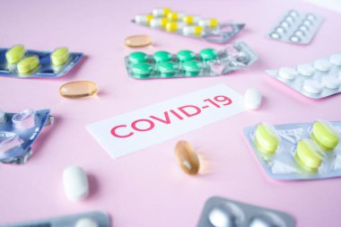 Pembe arka planda bir sürü hap ve hapla birlikte covid-19 'dan alıntılar var. Coronavirus tedavisi konsepti. İlaçlar, virüs için aşılar. Antibiyotikler