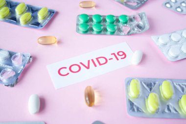Pembe arka planda bir sürü hap ve hapla birlikte covid-19 'dan alıntılar var. Coronavirus tedavisi konsepti. İlaçlar, virüs için aşılar. Antibiyotikler