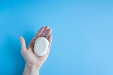 Bir erkeğin elindeki bir sabun parçası mavi arka planda üst bir görüntü. İnsan eli sabun tutar. Ellerini yıka. Bakteri ve virüslere karşı sabun. Koronavirüsle savaşmak için hijyen ve kısırlığa uyum.