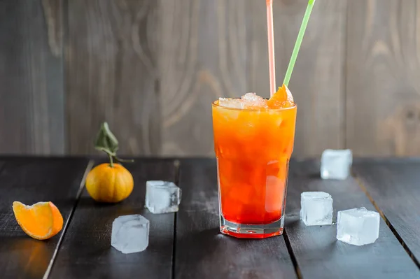 Bebida de coquetel laranja fresca com cubos de gelo em fundo de madeira preta — Fotografia de Stock