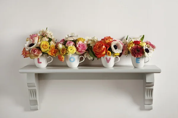 colorful flower arrangements in four cups showing the letters LO
