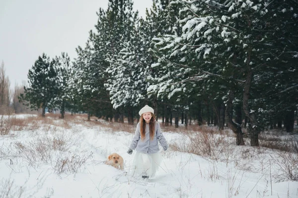 Menina brincando com neve na floresta com o cão Labrador — Fotografia de Stock