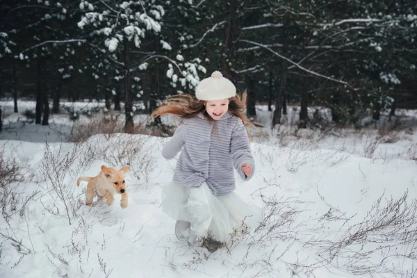 Menina brincando com neve na floresta com o cão Labrador — Fotografia de Stock